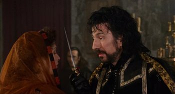 Movie still from “Robin Hood: Prince of Thieves” (1991), directed by Kevin Reynolds – A man holding a sword in front of a woman; Close Up shot, Over the shoulder angle