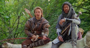 Movie still from “Robin Hood: Prince of Thieves” (1991), directed by Kevin Reynolds – Two men dressed in medieval costumes sitting on a wall; Medium shot, Low angle