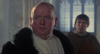 Movie still from “Robin Hood: Prince of Thieves” (1991), directed by Kevin Reynolds – An older man wearing a fur coat in a room; Close Up shot, Over the shoulder angle