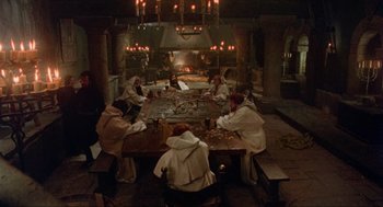 Movie still from “Robin Hood: Prince of Thieves” (1991), directed by Kevin Reynolds – A group of people sitting around a table in front of a fireplace; Wide shot, High angle