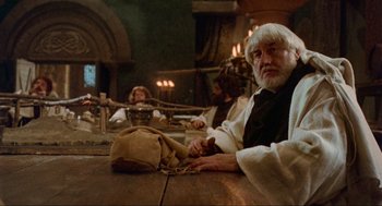 Movie still from “Robin Hood: Prince of Thieves” (1991), directed by Kevin Reynolds – A man sitting at a wooden table in a room; Medium shot, Over the shoulder angle