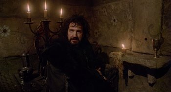 Movie still from “Robin Hood: Prince of Thieves” (1991), directed by Kevin Reynolds – A man sitting in a chair in front of candles; Medium shot, Over the shoulder angle
