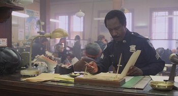 Movie still from “RoboCop” (1987), directed by Paul Verhoeven – A police officer is writing on a piece of paper; Medium shot, Low angle