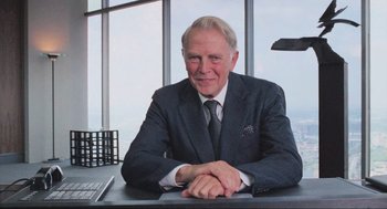 Movie still from “RoboCop” (1987), directed by Paul Verhoeven – An older man sitting at a desk in front of a window; Medium shot, Low angle