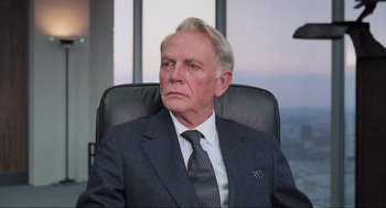 Movie still from “RoboCop” (1987), directed by Paul Verhoeven – An older man wearing a suit and tie sitting in an office chair looking pensive; Close Up shot, Low angle