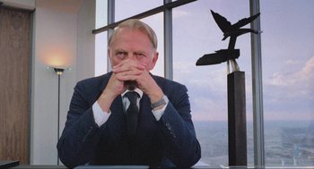 Movie still from “RoboCop” (1987), directed by Paul Verhoeven – A man in a suit and tie sitting in front of a window; Close Up shot, Low angle