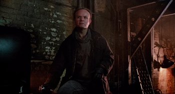 Movie still from “RoboCop” (1987), directed by Paul Verhoeven – A man standing in a dark room with his hands in his pockets; Medium shot, Low angle