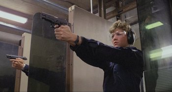 Movie still from “RoboCop” (1987), directed by Paul Verhoeven – A woman is holding a gun and wearing ear muffs; Medium shot, Low angle