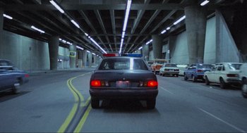 Movie still from “RoboCop” (1987), directed by Paul Verhoeven – A police car driving down a street under an overpass; Wide shot, High angle