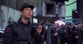 Movie still from “RoboCop” (1987), directed by Paul Verhoeven – A man holding a camera in front of a group of people; Medium shot, Low angle