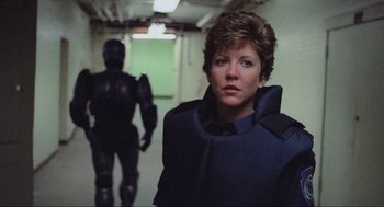 Movie still from “RoboCop” (1987), directed by Paul Verhoeven – A woman in a blue jacket standing next to a man in a black suit; Close Up shot, Over the shoulder angle