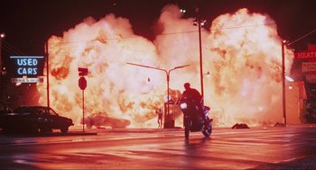 Movie still from “RoboCop” (1987), directed by Paul Verhoeven – A man riding a motorcycle down a street near a fire; Extreme Wide shot, High angle