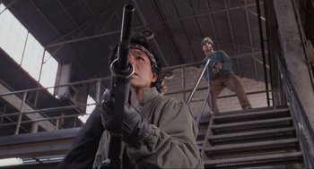 Movie still from “RoboCop” (1987), directed by Paul Verhoeven – A man holding a rifle while standing next to another man on stairs; Medium shot, Low angle