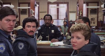 Movie still from “RoboCop” (1987), directed by Paul Verhoeven – A group of people sitting in front of a police officer; Medium shot, Low angle