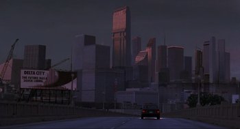 Movie still from “RoboCop” (1987), directed by Paul Verhoeven – A car driving down a street in front of tall buildings; Extreme Wide shot, Low angle