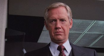 Movie still from “RoboCop” (1987), directed by Paul Verhoeven – An older man in a suit and tie looking at the camera; Close Up shot, Low angle