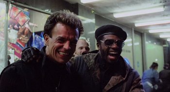 Movie still from “RoboCop” (1987), directed by Paul Verhoeven – Two men smiling for the camera in a room; Close Up shot, Low angle