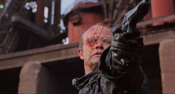 Movie still from “RoboCop” (1987), directed by Paul Verhoeven – A man with a broken eye is holding something in his hand; Close Up shot, Low angle