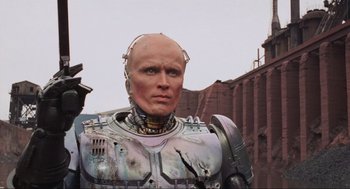 Movie still from “RoboCop” (1987), directed by Paul Verhoeven – A man in a metal suit standing in front of a brick building; Close Up shot, Low angle