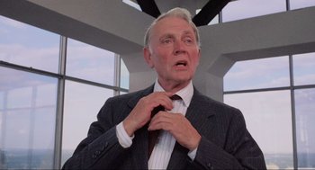 Movie still from “RoboCop” (1987), directed by Paul Verhoeven – An older man adjusts his neck tie in front of a window; Close Up shot, Low angle