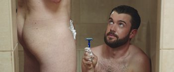 Movie still from “Robots” (2023), directed by Casper Christensen – A man shaving in front of a mirror with a razor; Medium shot, Over the shoulder angle