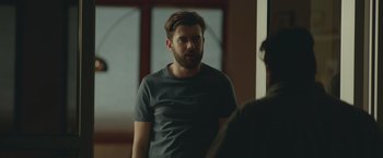 Movie still from “Robots” (2023), directed by Casper Christensen – A man in a gray shirt is talking to another man in front of a window; Medium shot, Over the shoulder angle