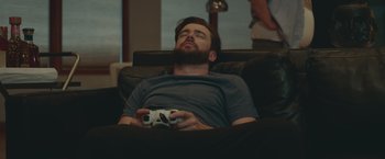 Movie still from “Robots” (2023), directed by Casper Christensen – A man is laying on a couch holding a game controller; Medium shot, High angle