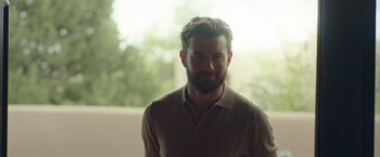 Movie still from “Robots” (2023), directed by Casper Christensen – A man with a goatee and a beard is smiling; Close Up shot, Over the shoulder angle