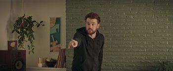 Movie still from “Robots” (2023), directed by Casper Christensen – A man in a black hoodie pointing at the camera; Medium shot, Over the shoulder angle