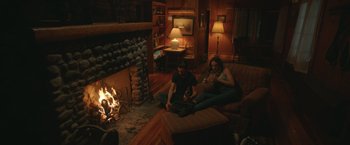Movie still from “Robots” (2023), directed by Casper Christensen – A man and a woman sitting in front of a fireplace; Wide shot, High angle