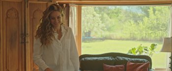 Movie still from “Robots” (2023), directed by Casper Christensen – A woman standing in front of a window with a couch in the background; Medium shot, Over the shoulder angle