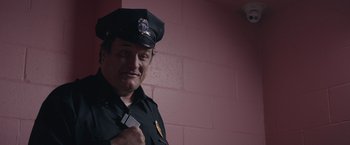 Movie still from “Robots” (2023), directed by Casper Christensen – A man in a police officer's uniform holding a pair of scissors; Close Up shot, Low angle