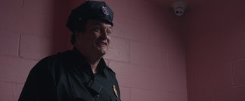 Movie still from “Robots” (2023), directed by Casper Christensen – A man in a police uniform smiles for the camera; Close Up shot, Low angle