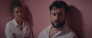 Movie still from “Robots” (2023), directed by Casper Christensen – A man with a beard is sitting in a pink room; Close Up shot, Over the shoulder angle