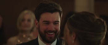 Movie still from “Robots” (2023), directed by Casper Christensen – A person wearing a suit and smiling; Close Up shot, Over the shoulder angle