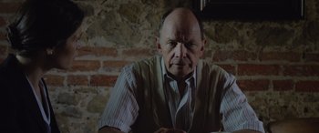 Movie still from “Rogue Agent” (2022), directed by Adam Patterson – An older man sitting in front of a brick wall; Close Up shot, Low angle