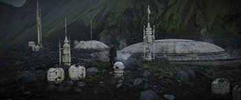 Movie still from “Rogue One: A Star Wars Story” (2016), directed by Gareth Edwards – A man standing on a rocky ground next to a building; Extreme Wide shot, High angle