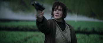 Movie still from “Rogue One: A Star Wars Story” (2016), directed by Gareth Edwards – A woman is holding a gun in a field; Close Up shot, Over the shoulder angle