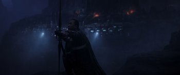 Movie still from “Rogue One: A Star Wars Story” (2016), directed by Gareth Edwards – A man holding a bow and arrow in the dark; Medium shot, Over the shoulder angle