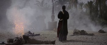 Movie still from “Rogue One: A Star Wars Story” (2016), directed by Gareth Edwards – A man standing in the sand near a fire pit; Wide shot, Over the shoulder angle