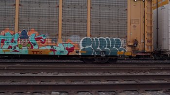 Movie still from “Rolling Like Thunder” (2021), directed by Roger Gastman – A train car covered in graffiti on the side of the tracks; Wide shot, Low angle