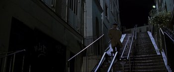 Movie still from “Ronin” (1998), directed by John Frankenheimer – A man walking down a set of stairs in the dark; Wide shot, Low angle