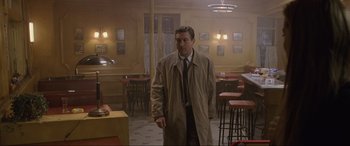 Movie still from “Ronin” (1998), directed by John Frankenheimer – A man wearing a trench coat in a restaurant; Wide shot, High angle
