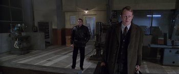 Movie still from “Ronin” (1998), directed by John Frankenheimer – Two men standing next to each other in a building; Medium shot, Low angle