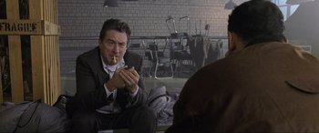 Movie still from “Ronin” (1998), directed by John Frankenheimer – A man sitting down with a cigarette in his mouth; Medium shot, Low angle