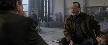 Movie still from “Ronin” (1998), directed by John Frankenheimer – A man sitting on the ground talking to another man; Medium shot, Over the shoulder angle