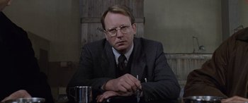 Movie still from “Ronin” (1998), directed by John Frankenheimer – A man sitting at a table in a suit and tie; Close Up shot, Low angle