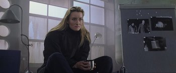 Movie still from “Ronin” (1998), directed by John Frankenheimer – A woman sitting on the ground holding a cup; Medium shot, Low angle