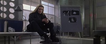 Movie still from “Ronin” (1998), directed by John Frankenheimer – A woman sitting on top of a chair holding a cup; Medium shot, Low angle