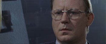 Movie still from “Ronin” (1998), directed by John Frankenheimer – A person wearing a suit and glasses; Close Up shot, Over the shoulder angle
